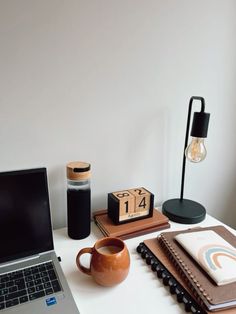 an open laptop computer sitting on top of a desk next to a cup and notebook