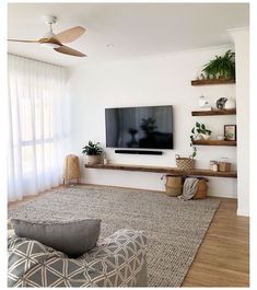 a flat screen tv sitting on top of a wooden shelf in a living room next to a window