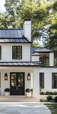 a large white house with black doors and windows on the front door is surrounded by greenery