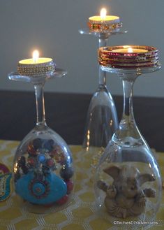 two wine glasses with candles in them sitting next to each other on a yellow table cloth