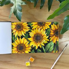 an open notebook with sunflowers on it next to some leaves and a pencil