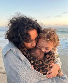 a woman holding a child wrapped in a blanket on top of a beach next to the ocean