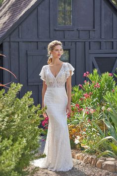 a woman in a white wedding dress walking down a path near some flowers and plants