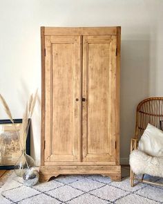 a wooden armoire sitting next to a wicker chair in a room with white walls