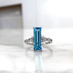 a ring with an emerald colored stone surrounded by white diamonds on a marble countertop