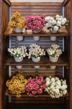 flowers are arranged in white and pink vases on wooden shelve with wood slats behind them