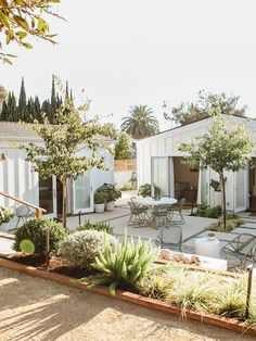 an outdoor patio with tables and chairs surrounded by plants, trees, and other greenery