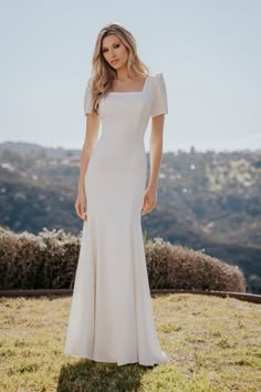 a woman in a white dress standing on top of a grass covered field