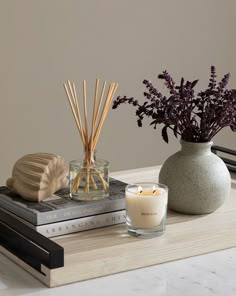 an arrangement of candles, flowers and books on a table with a vase in the background