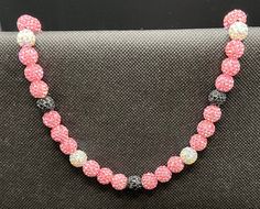 a pink beaded necklace is displayed on a black cloth surface, with silver beads