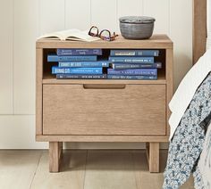 a nightstand with books on top of it next to a bowl and eyeglasses