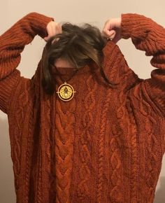 a woman with her hands on her head wearing an orange sweater