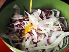 someone pouring dressing into a green bowl filled with shredded red and white cabbage salad ingredients