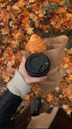 a person holding a cupcake in their hand and some leaves on the ground behind them