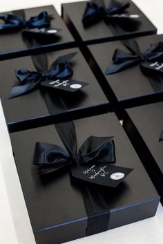 four black gift boxes with ribbons tied around the edges and tags on each one side