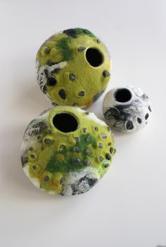 three vases with holes in them sitting on a white surface, one is green and the other is black