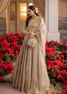 a woman standing in front of red flowers wearing a beige lehenga with matching blouse and dupatta