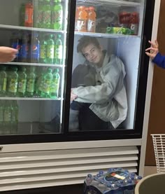 a man standing in front of a refrigerator filled with water and sodas next to another person