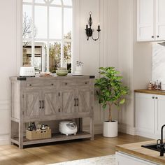 a kitchen with white cabinets and wood flooring next to a potted plant on the counter