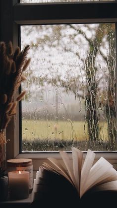 an open book sitting on top of a table next to a window covered in rain