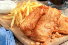 two pieces of fish and fries on a cutting board