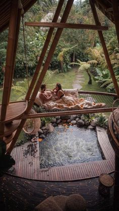 two people are laying in a hot tub surrounded by greenery and bamboo structures that surround the pool