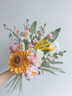 a hand holding a crocheted flower bouquet with yellow and white flowers on it