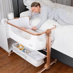 a woman laying in bed next to a white crib with a baby in it