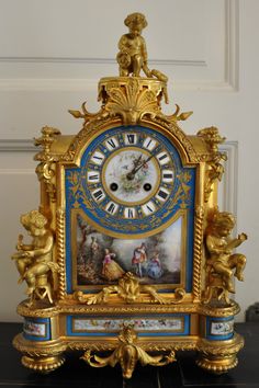 an ornate gold and blue clock with cherubs on the face, sitting on a black table