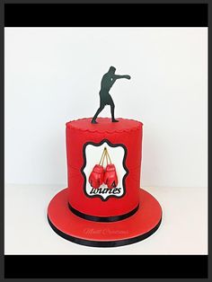 a red cake with a man standing on top of it and boxing gloves in the shape of a ring