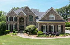 a large brick house with lots of windows and bushes in front of it on a sunny day