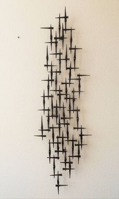 a sculpture made out of metal rods on a white wall next to a black clock