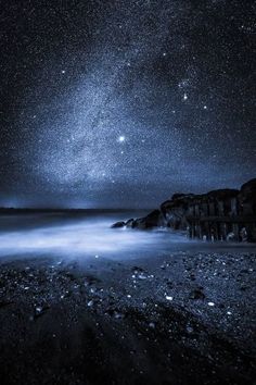 the night sky is filled with stars and some water in front of an ocean shore