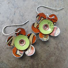 two orange and green flower shaped earrings sitting on top of a stone floor next to each other