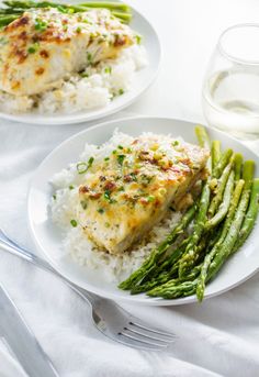 two white plates topped with fish and rice next to asparagus on a table