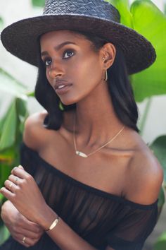 a woman in a black dress and hat posing for the camera with her hand on her chest