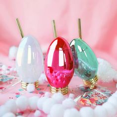 three different colored vases sitting on top of a pink surface with confetti