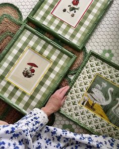 a person's hand is pointing at four framed pictures on the floor with animals and flowers