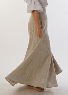 Opulent and graceful, the high-waisted linen maxi skirt catches the eye with irresistible modernity. Its asymmetric fastening, decorated with coconut buttons, adds a touch of freshness and exoticism. But what makes it truly unique are the hidden pockets, skillfully integrated into the seams, which combine practicality and style.  The skirt presents the natural color of linen, emphasizing its natural beauty. Its clean design perfectly hides any imperfections on the body, restoring harmony and cor Beige Buttoned Long Skirt, Beige Long Skirt With Buttons, Elegant Linen Bottoms With Buttons, Solid Color Linen Flared Skirt, Fitted Beige Linen Maxi Skirt, Beige Linen Long Skirt, Beige Linen Wide Leg Maxi Skirt, Victorian Walking Skirt, Walking Skirt