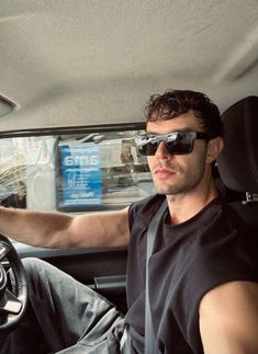 a man wearing sunglasses sitting in the driver's seat of a car