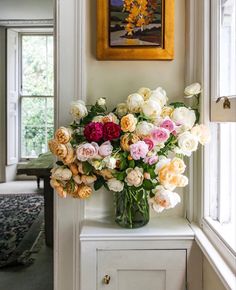 a vase filled with lots of flowers sitting on top of a white table next to a window