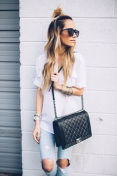 a woman in white shirt and jeans holding a black purse with her hand on her hip