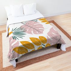 a bed covered in a pink and green leaf print comforter set on top of a wooden floor