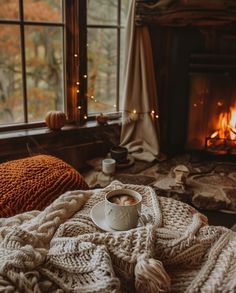 a cup of coffee sits on a blanket in front of a fireplace