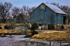 an old blue barn sits in the middle of a field next to a small pond