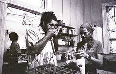 two people standing in a kitchen with bottles and utensils on the counter top