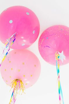 three pink balloons with streamers and confetti on them, against a white background