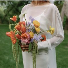 a woman holding a bouquet of flowers in her hands and wearing a white dress with long sleeves