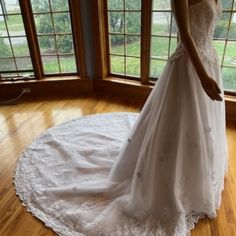 a woman in a white wedding dress is standing on a wooden floor near large windows