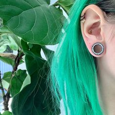 a woman with green hair wearing ear piercings and an earring on her left ear